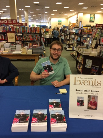 Writer Randal Eldon Greene holding a copy of his literary fiction novel Descriptions of Heaven.